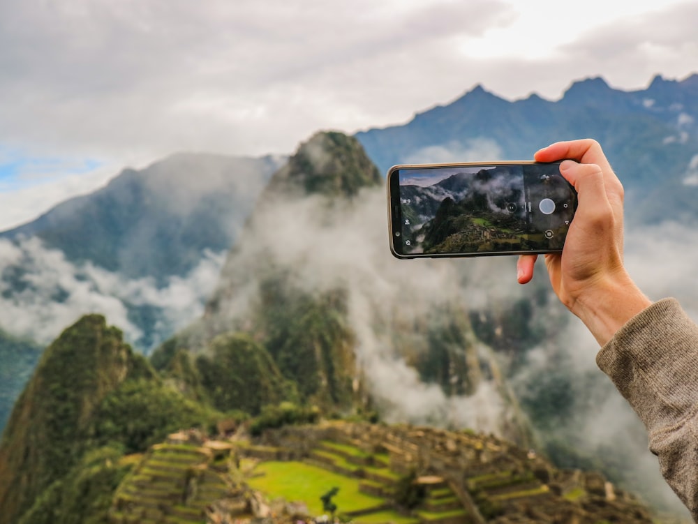 Persona che tiene lo smartphone che scatta foto della montagna verde