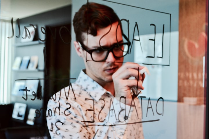 man writing on a clear dry erase board and connecting different points with arrows in a office  