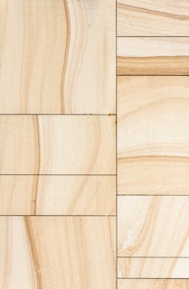 Rectangular sandstone tiles with natural beige and tan veining are arranged in a grid pattern. The tiles exhibit subtle variations in texture and color, creating a harmonious natural design.