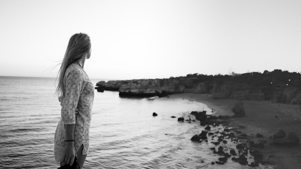 donna in piedi sulla fotografia in scala di grigi della riva del mare