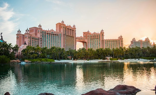 برج‌های صورتی هتل آتلانتیس با پل میان دو برج، پشت نخل‌ها و تالاب هنگام غروب