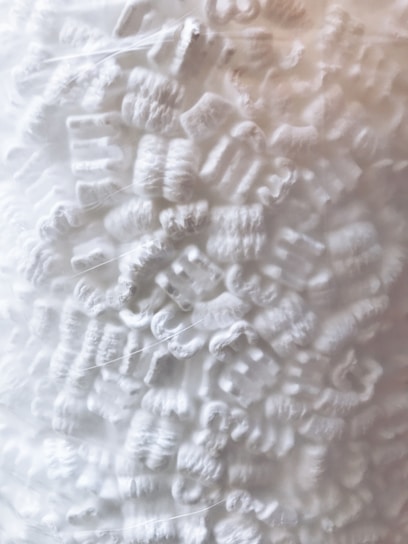 Close-up view of a collection of white packing peanuts. The packing material has a curly and irregular shape, filling the entire frame with a textured and foamy appearance.