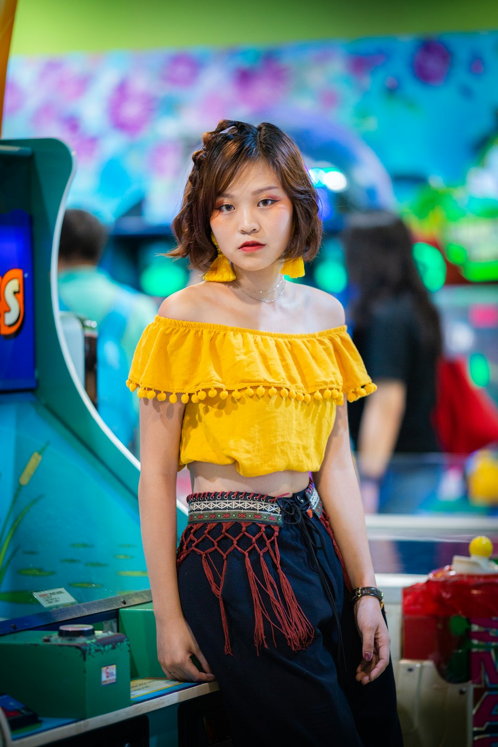 woman in yellow off-shoulder crop top sitting on green and blue arcade machine