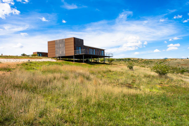 A modern manufactured home nestled in a green rural landscape under a clear blue sky.