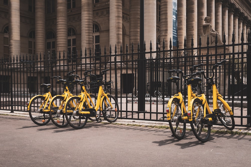 gelbe Fahrräder neben schwarzem Zaun