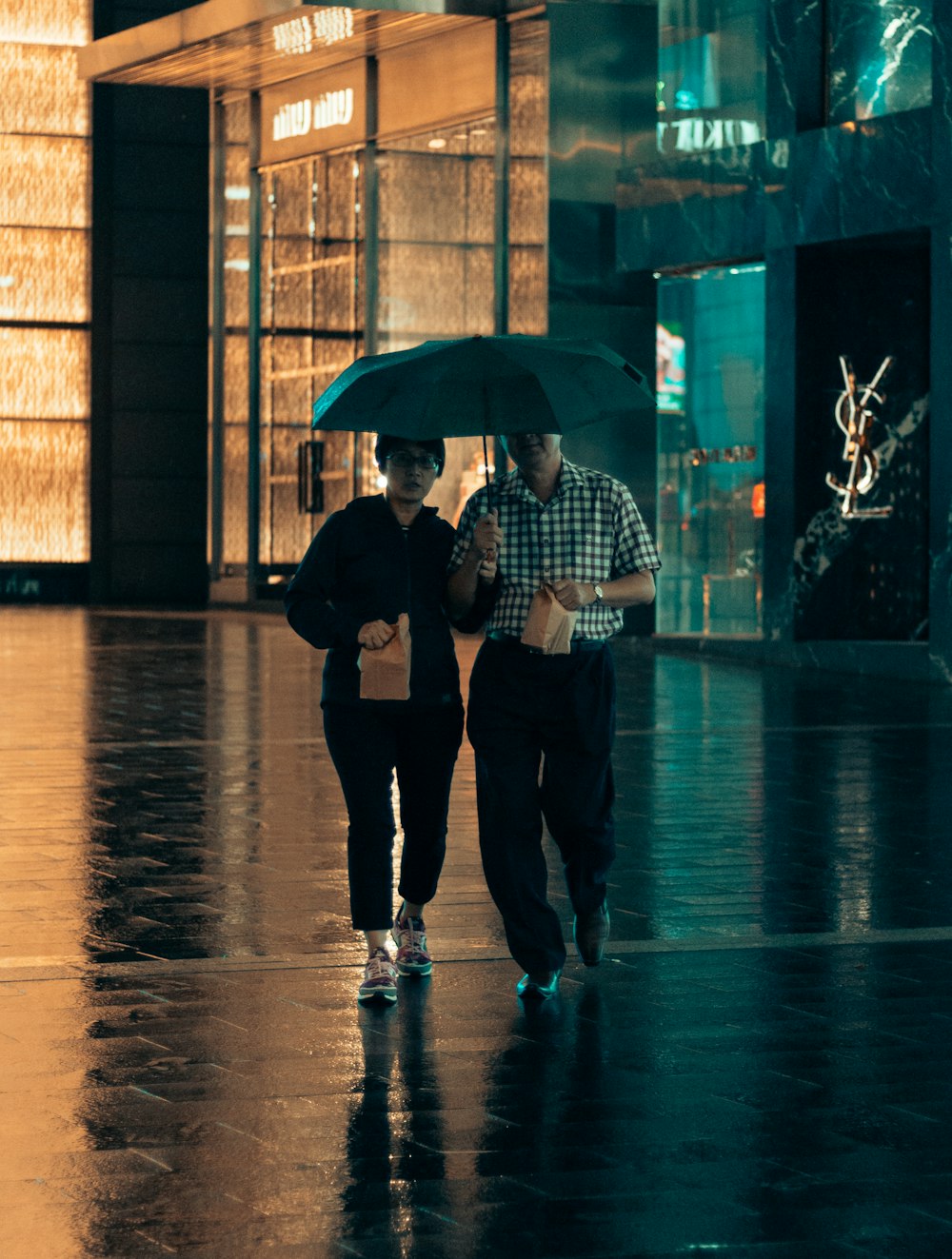 man and woman under same umbrella walking while holding paper bags