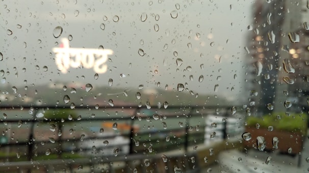 A cracked window with rain streaming down, blurred letters visible on the sill.