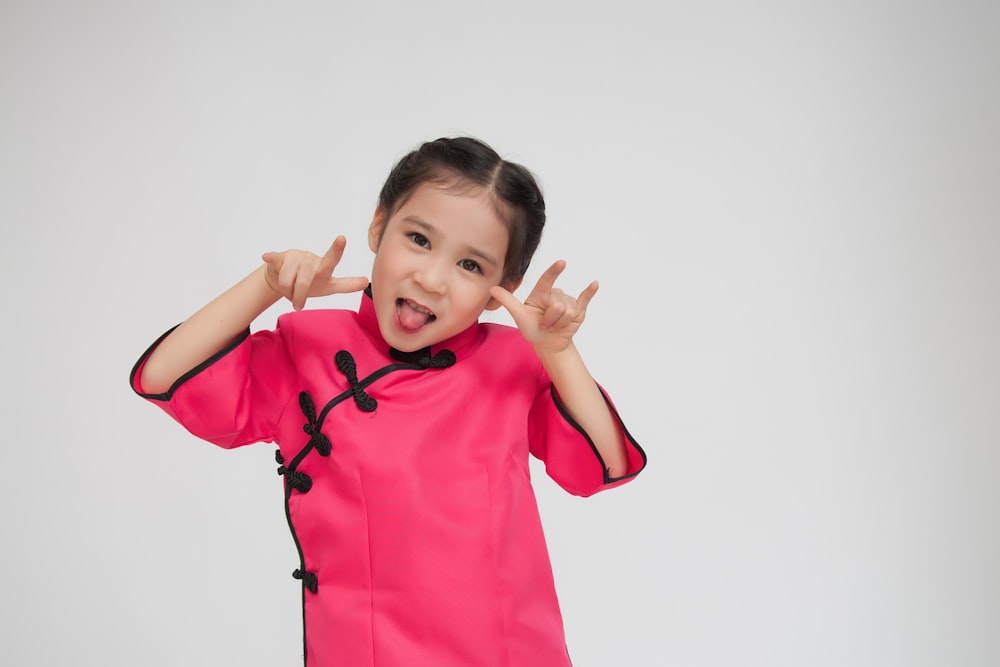 menina usando vestido cor-de-rosa que coloca a língua para fora com gestos das mãos