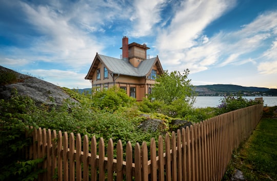 brown wooden house surrounded by fence near body of water in Drøbak Norway