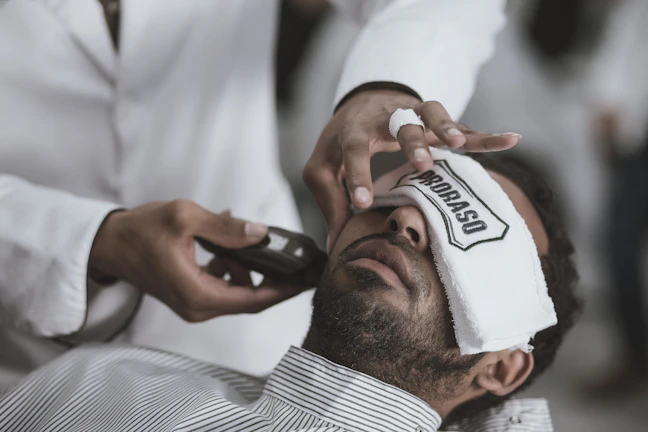 Barber applying hot towel treatment to a client's face, emphasizing personalized care.