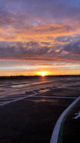 A panoramic shot of a vibrant sunset blending orange and violet above a quiet airfield.
