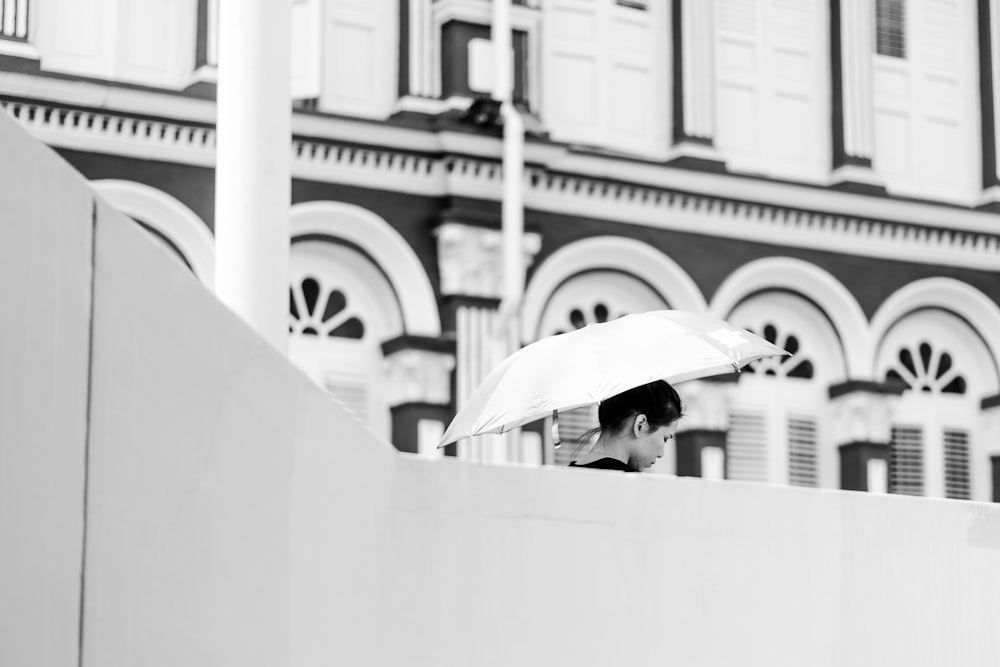 woman holding umbrella beside white concrete building