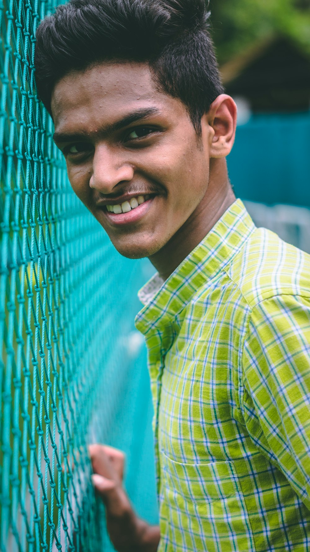 man wearing green collared top standing beside green cyclone fence
