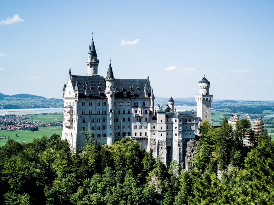 Majestic castle with multiple towers and spires perched atop a hill surrounded by lush greenery