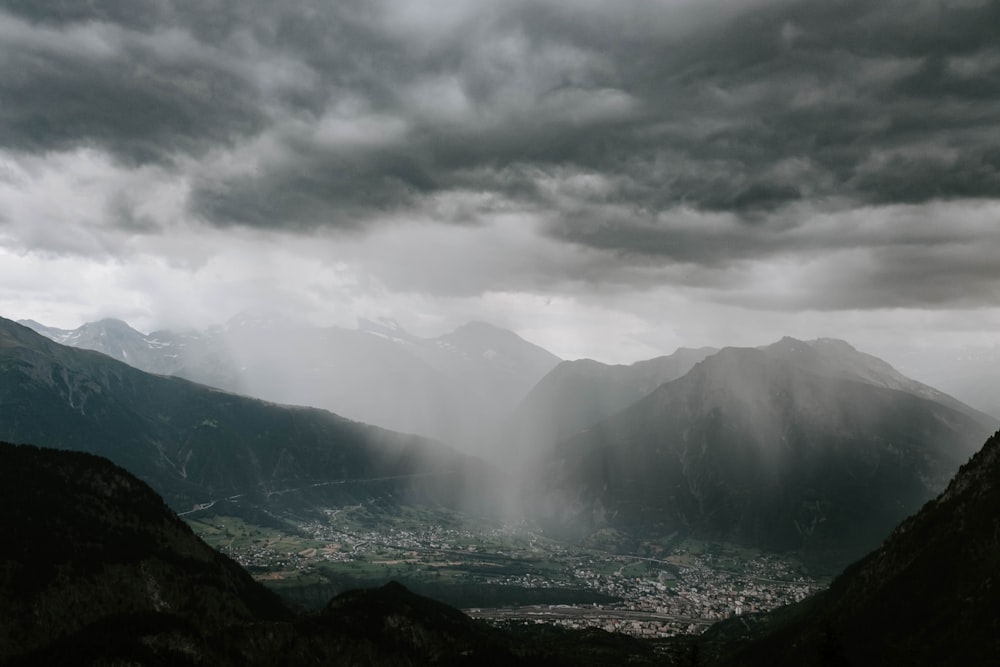fotografia aérea de cidades cercadas de montanha durante nuvens cinzentas