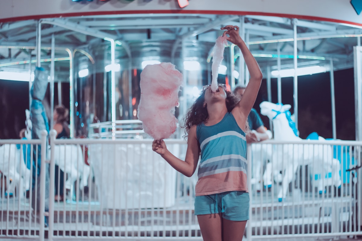 A woman enjoying pink cotton candy at a summer carnival &mdash; the kind of fun seasonal treat that defines summer snack season at Trader Joe's
