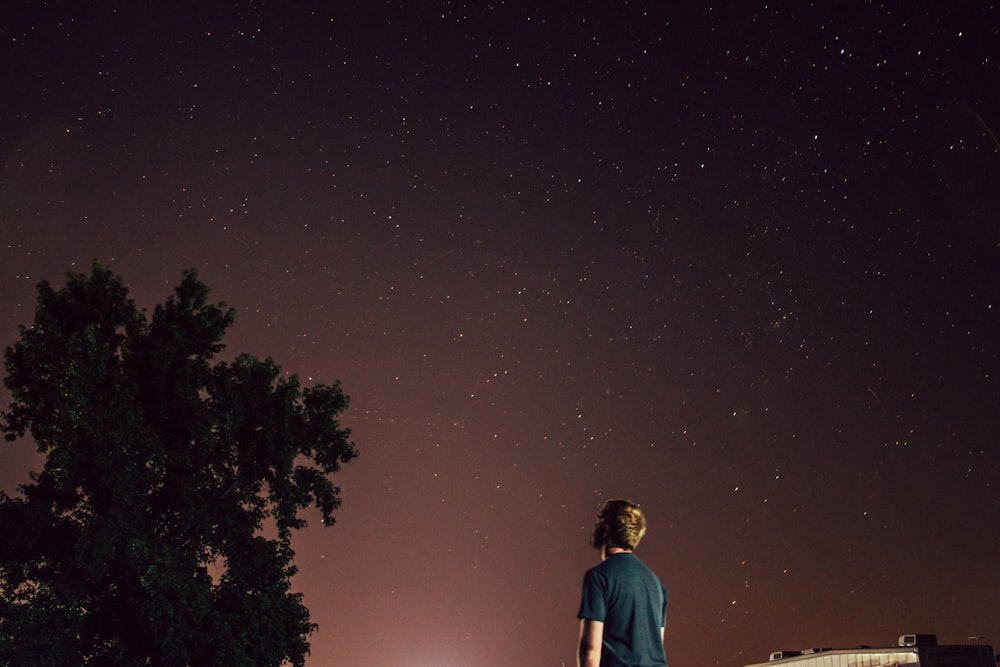 man standing beside tree under brown sky