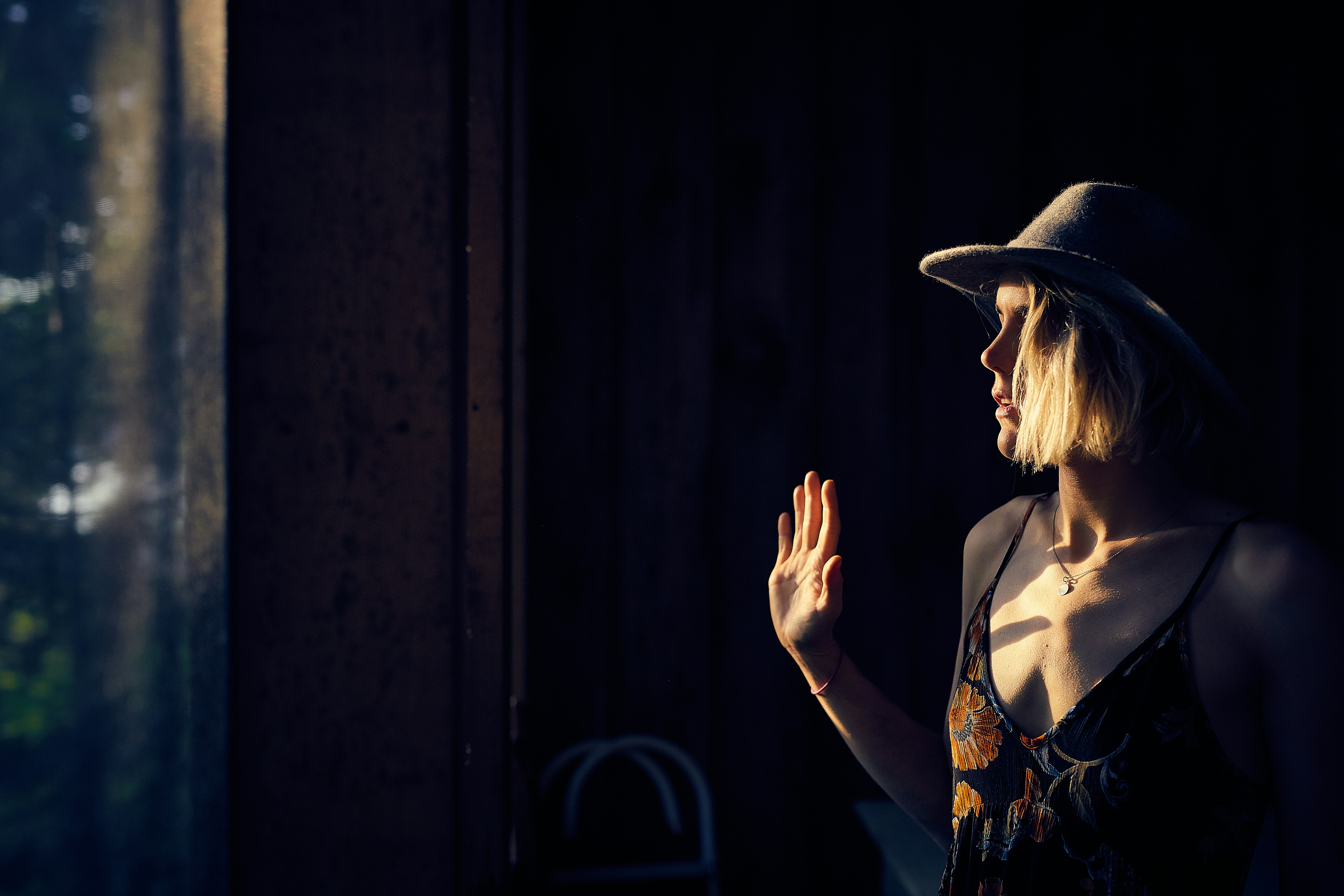 woman wearing brown floral spaghetti-strap dress standing beside window