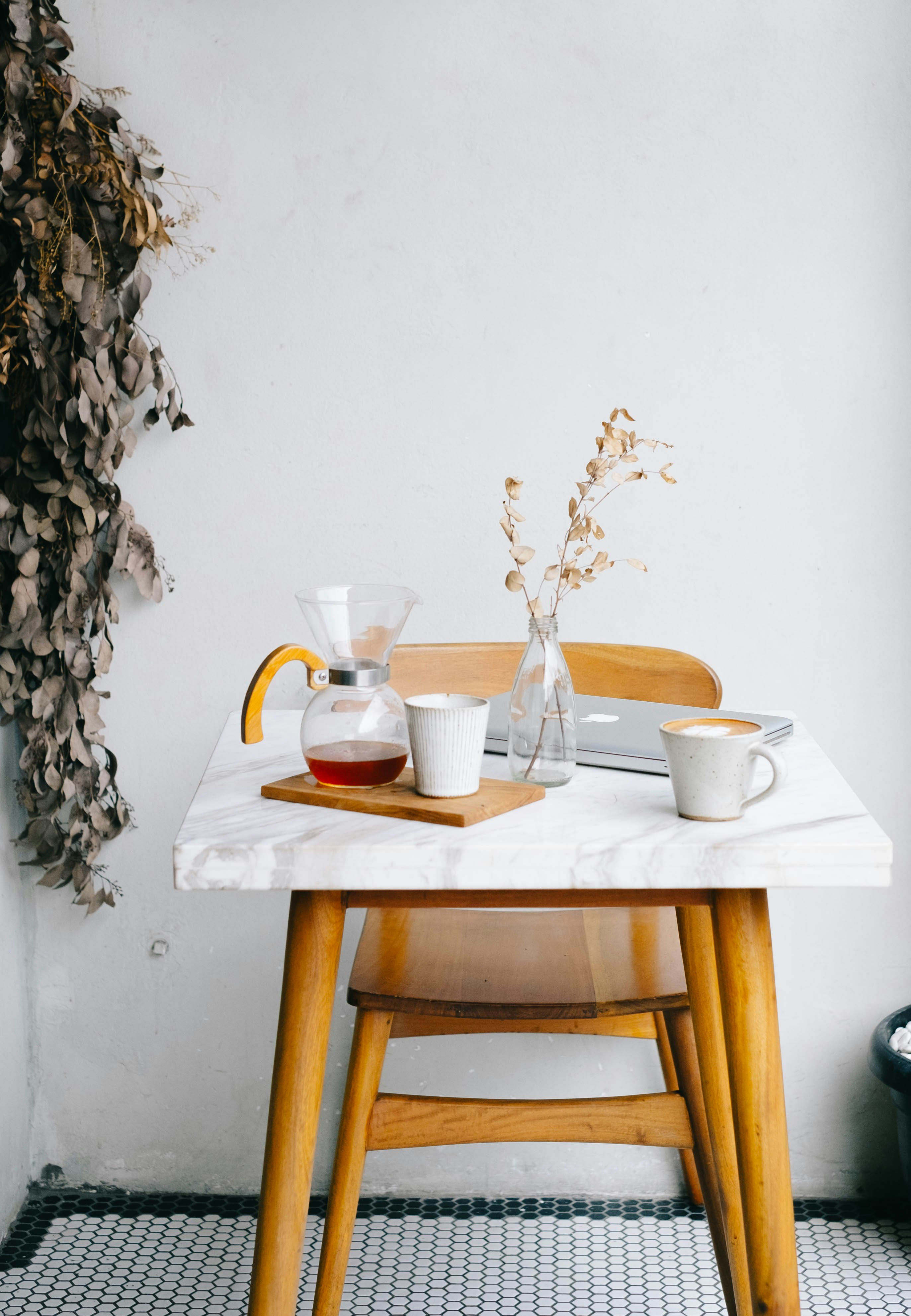 white ceramic mugs, clear glass pitcher and vase, and silver MacBook on top of white and brown table