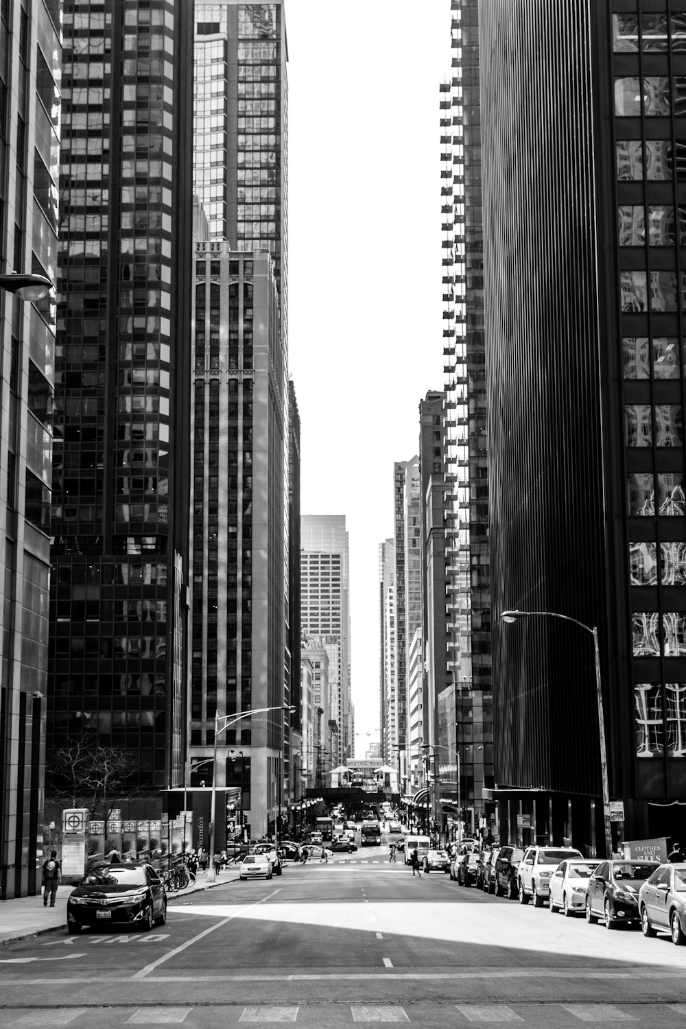 grayscale photo of road in between of tall buildings with vehicles
