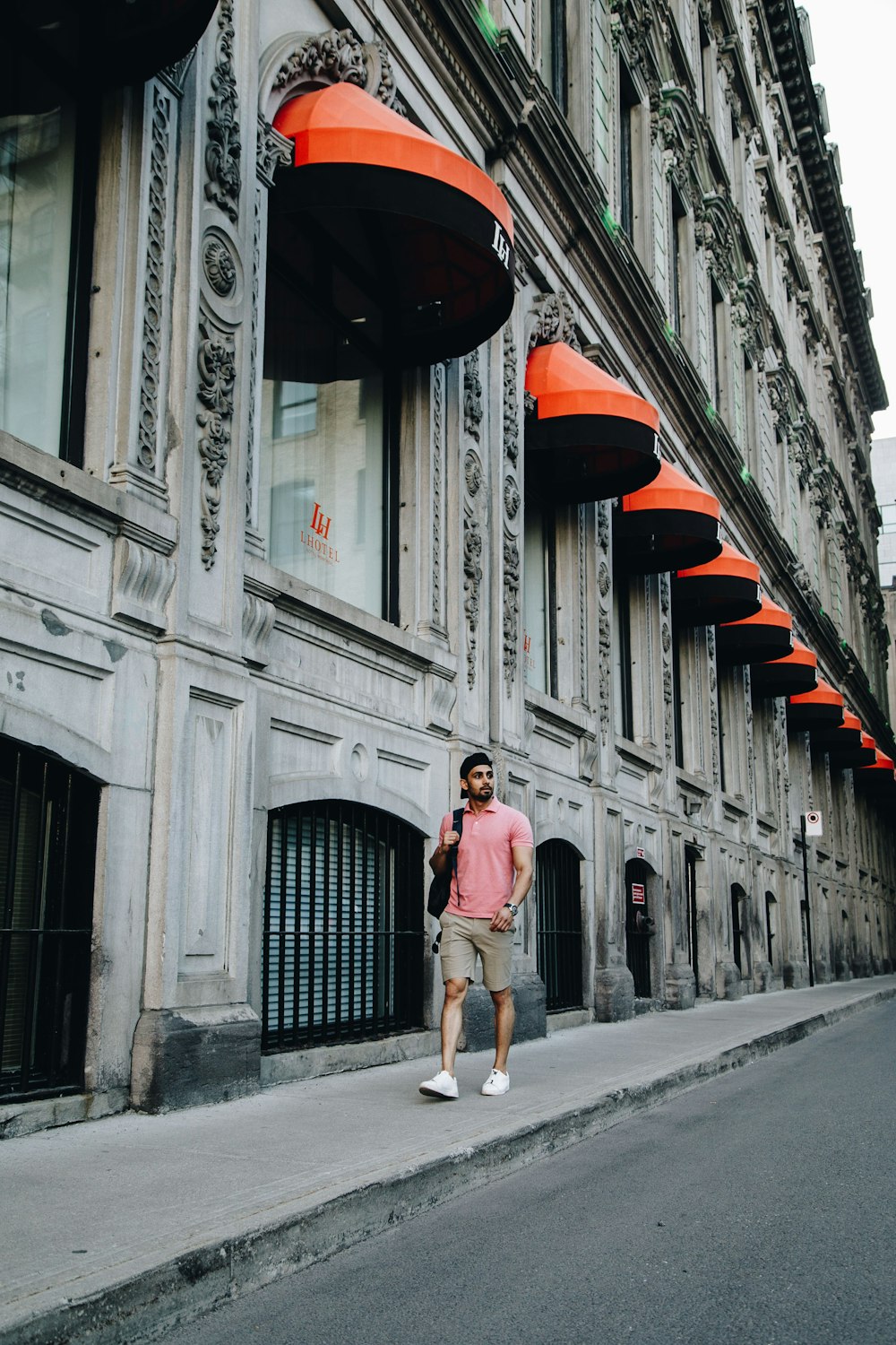 uomo che indossa una polo rosa che cammina accanto a un edificio in cemento grigio