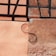 A segment of a building wall that displays a mix of textures and colors. The wall features two distinct plaster sections, one with a smooth peach tone and the other with a rougher, darker beige surface. Black wooden beams form a geometric pattern on the upper section. A curved metal rod resembling an 'S' shape is attached, adding an artistic element.