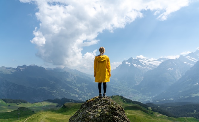 woman standing on rock in front of mountain during daytime