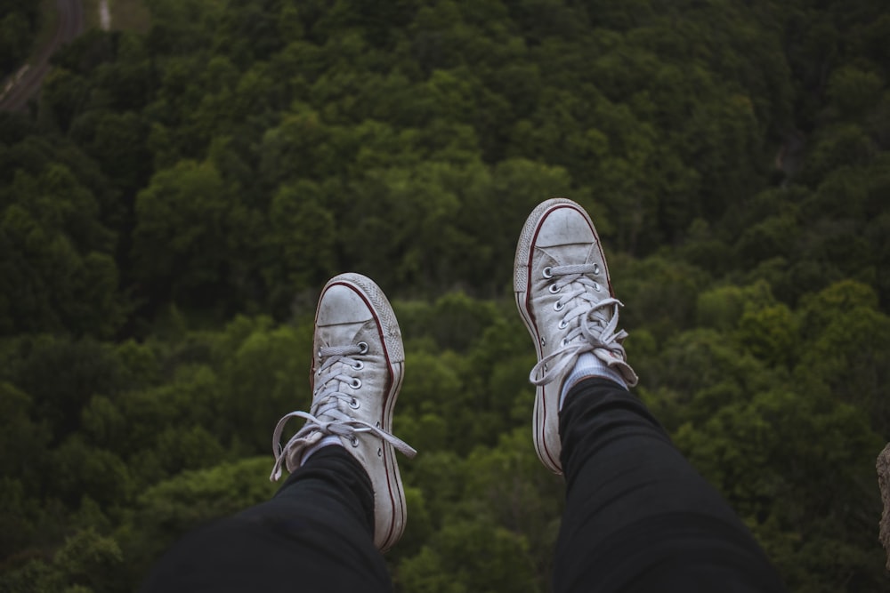 person sitting on cliff while wearing white shoes