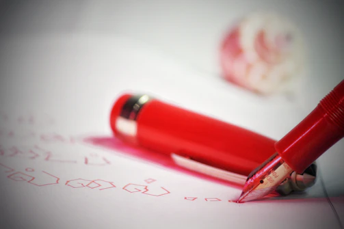 A close-up of a deep carmine red pen resting on crisp parchment, highlighting its elegant design.