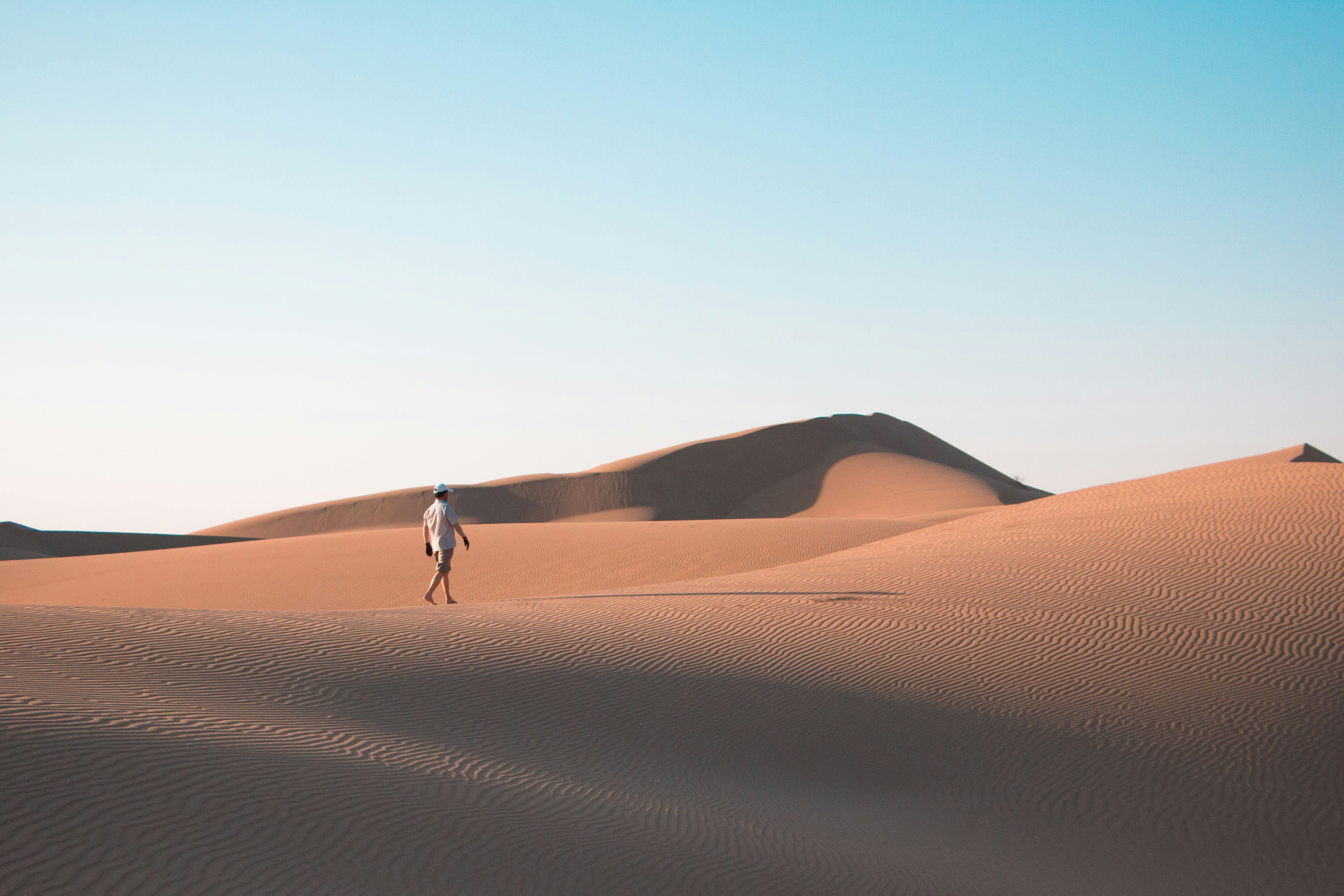 man walking on desert under blue sky during daytime