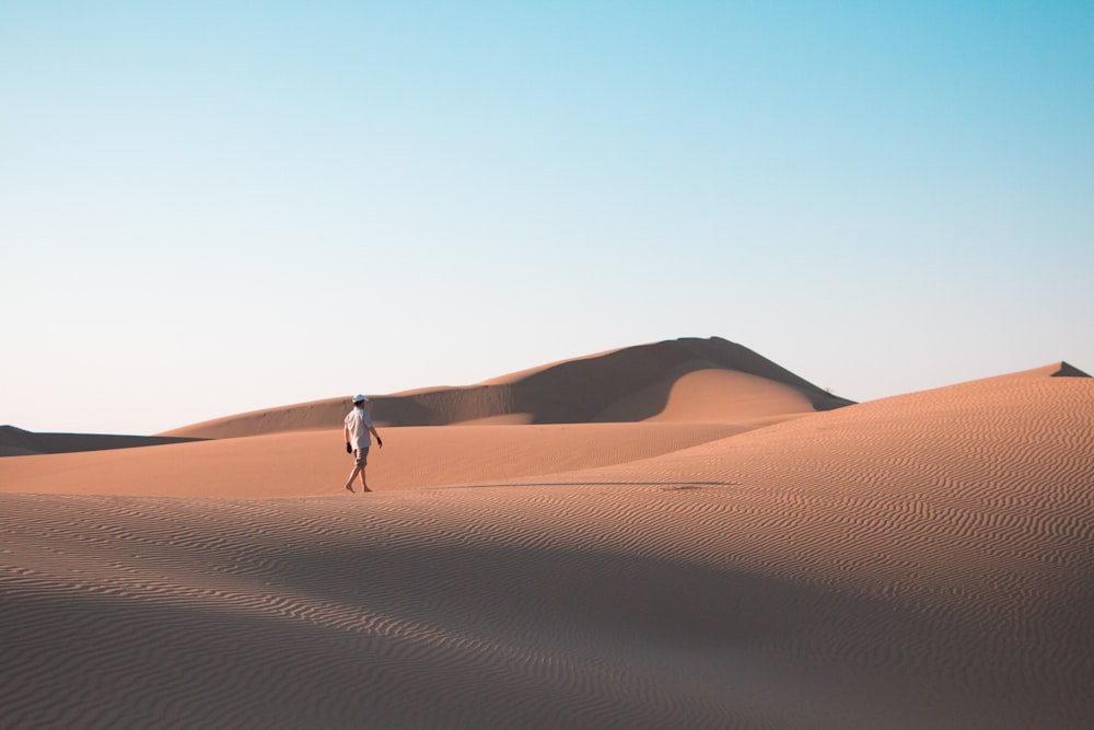 man walking on desert under blue sky during daytime