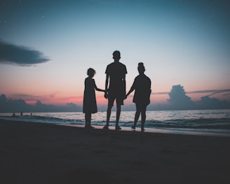 silhouette of three people walking beside body of water