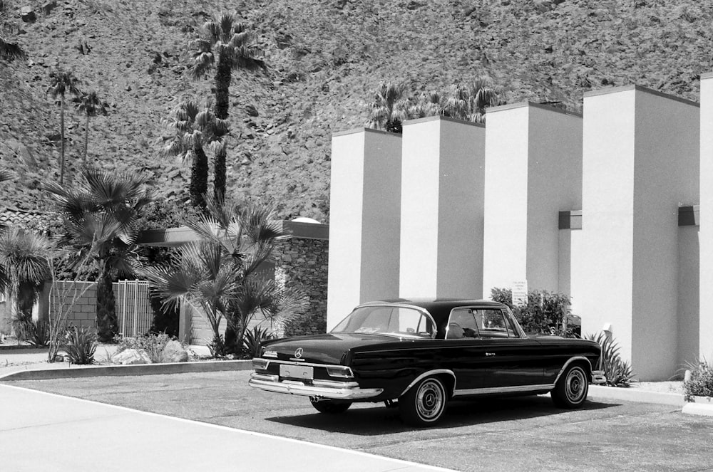 Graustufenfotografie eines grauen Coupés, das vor einem weißen Gebäude geparkt ist