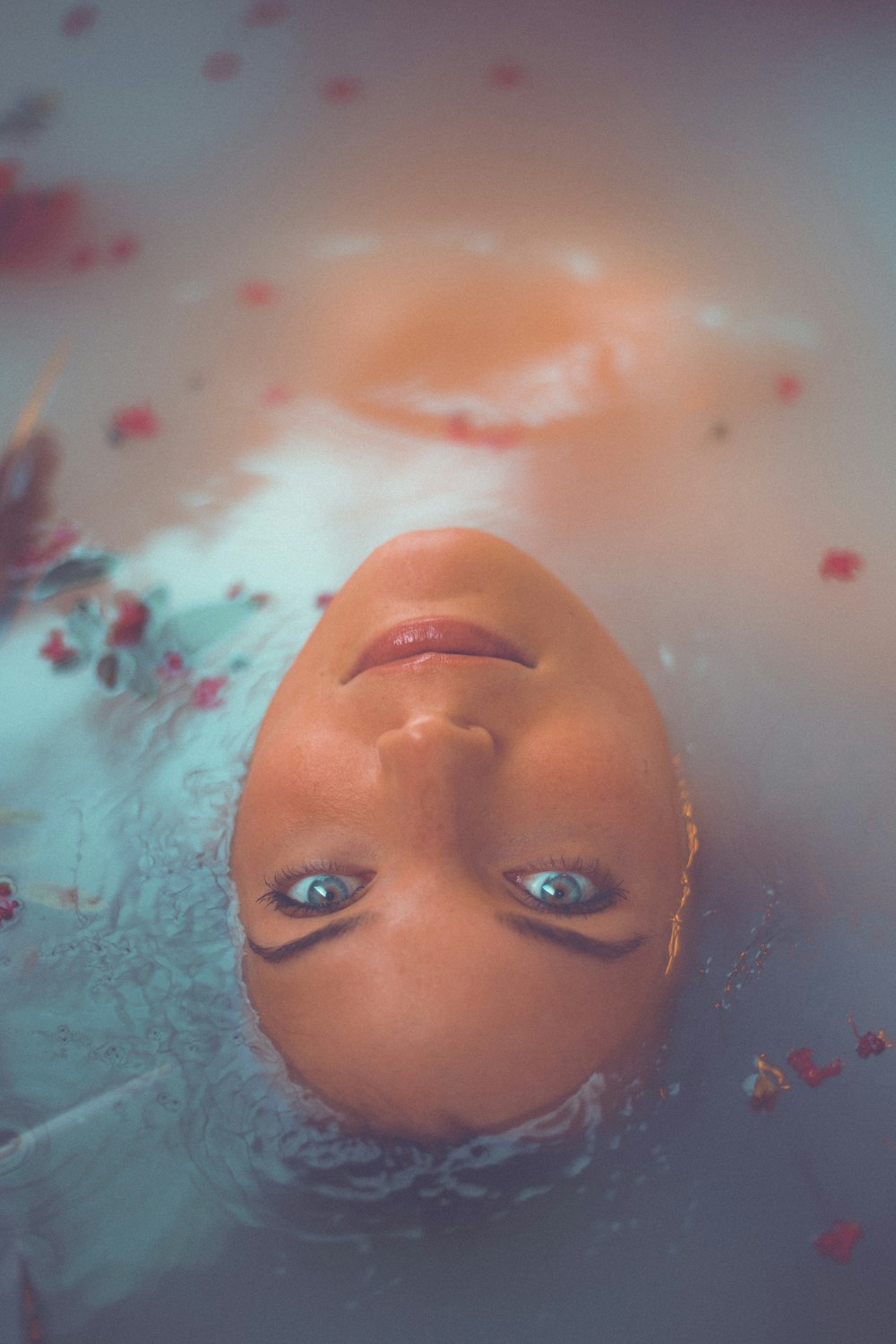 femme se baignant sur l’eau avec des pétales de fleurs rouges
