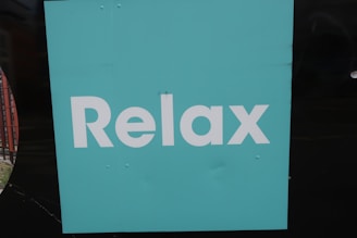 A turquoise square background with the word 'Relax' written in bold, white letters. The background is simple and plain, creating a minimalist appearance.