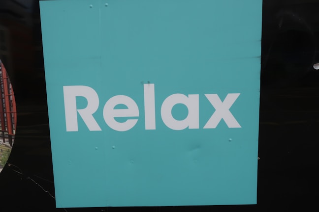 A turquoise square background with the word 'Relax' written in bold, white letters. The background is simple and plain, creating a minimalist appearance.