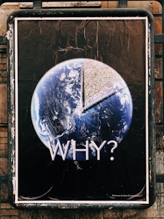 A poster featuring the Earth with a large portion removed, revealing a dry, cracked surface. The word 'WHY?' is prominently displayed underneath, suggesting a message about environmental concerns, such as climate change or deforestation. The image contrasts the planet’s vibrant blue and white colors against a stark brown, emphasizing the theme of environmental degradation.