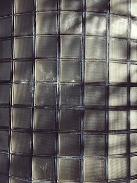 A grid pattern consisting of square glass blocks with textured surfaces, creating a repetitive and uniform layout. The lighting casts shadows and highlights across the tiles, giving the surface a subtle depth.