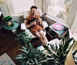 man sitting on sofa chair playing classic guitar