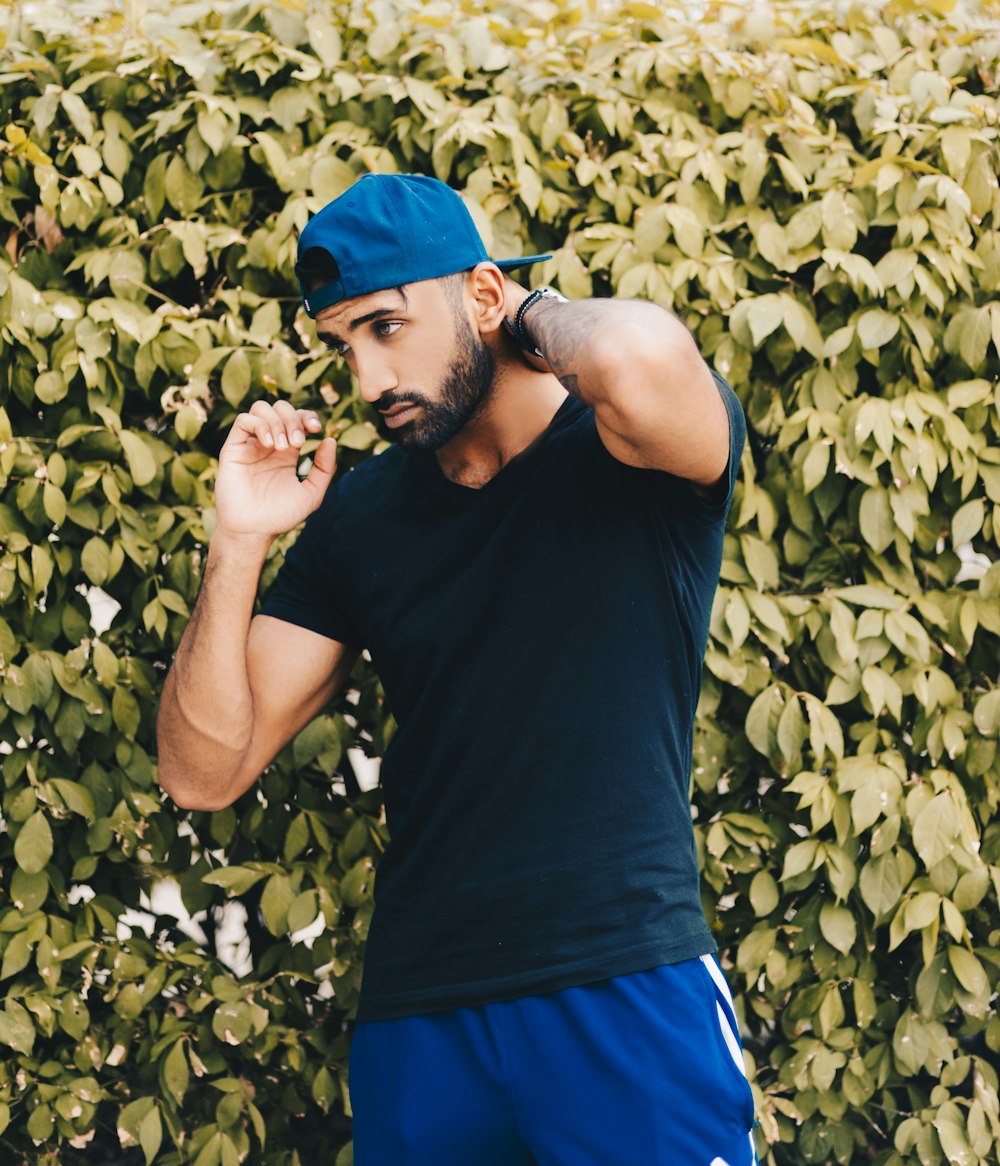 man wearing black V-neck t-shirt against green leafed wall