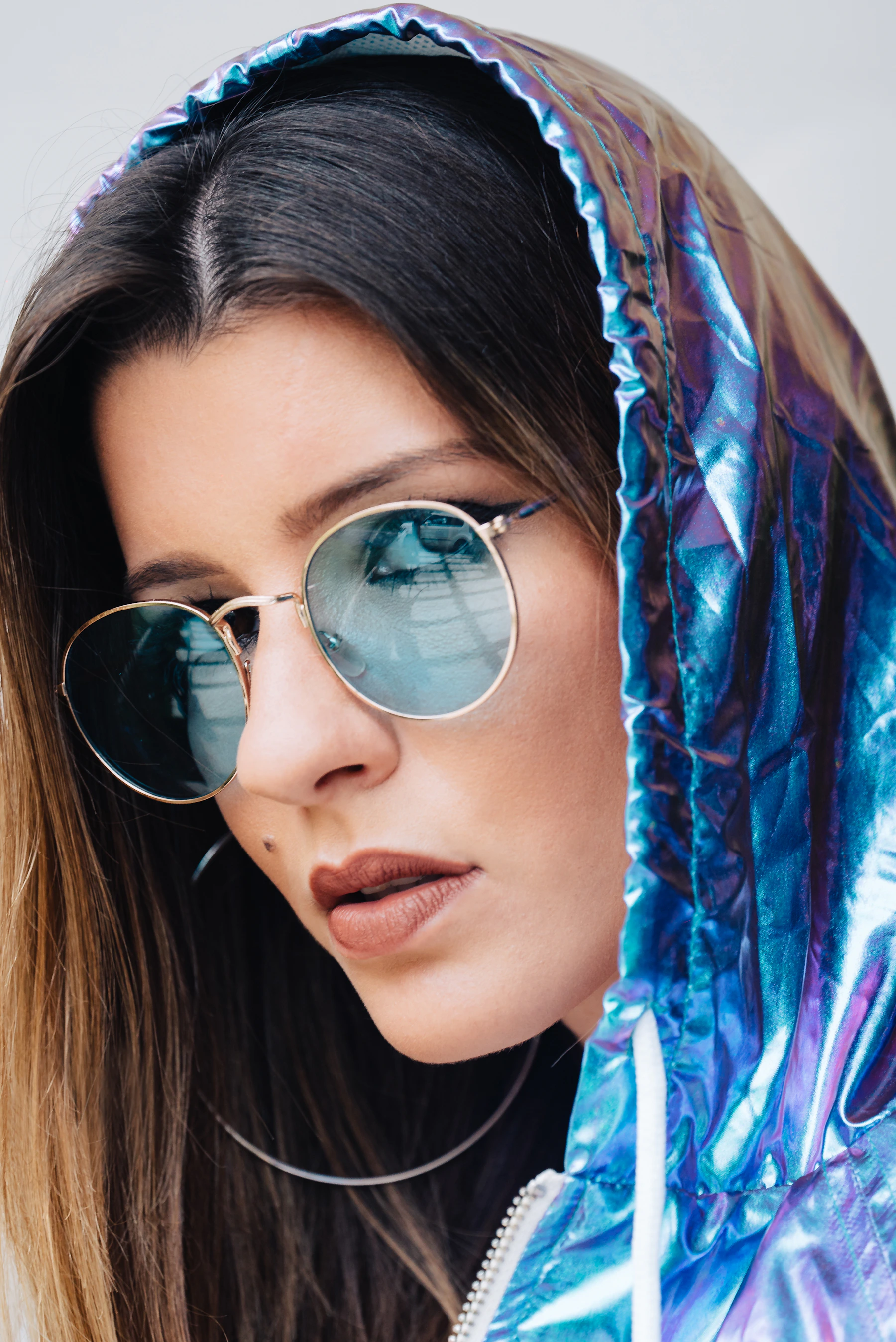 Woman wearing round blue mirrored sunglasses and a metallic blue hood