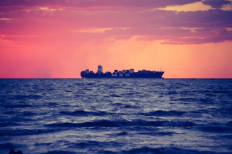 A cargo ship loaded with colorful containers sailing across a calm ocean at sunset.