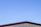 A simple structure with a metal roof against a clear blue sky. The roof has a maroon-colored edge, and the walls beneath appear to be light beige or cream-colored.