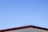 A simple structure with a metal roof against a clear blue sky. The roof has a maroon-colored edge, and the walls beneath appear to be light beige or cream-colored.