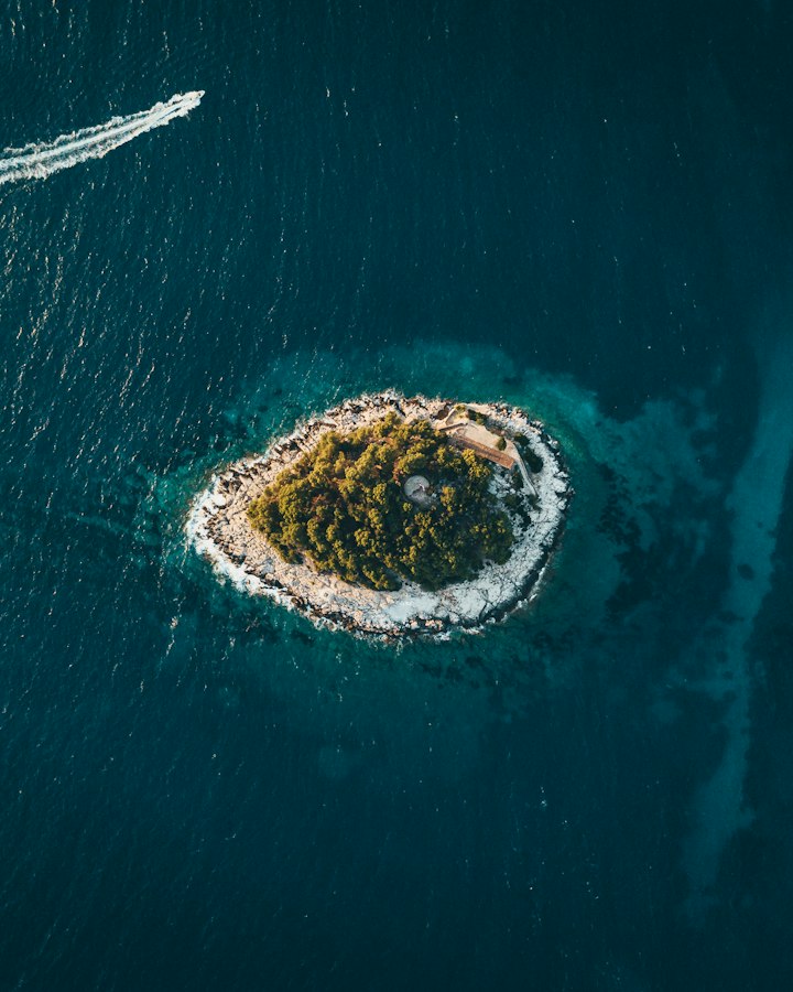 Aerial view of a small wooded island ringed by turquoise water