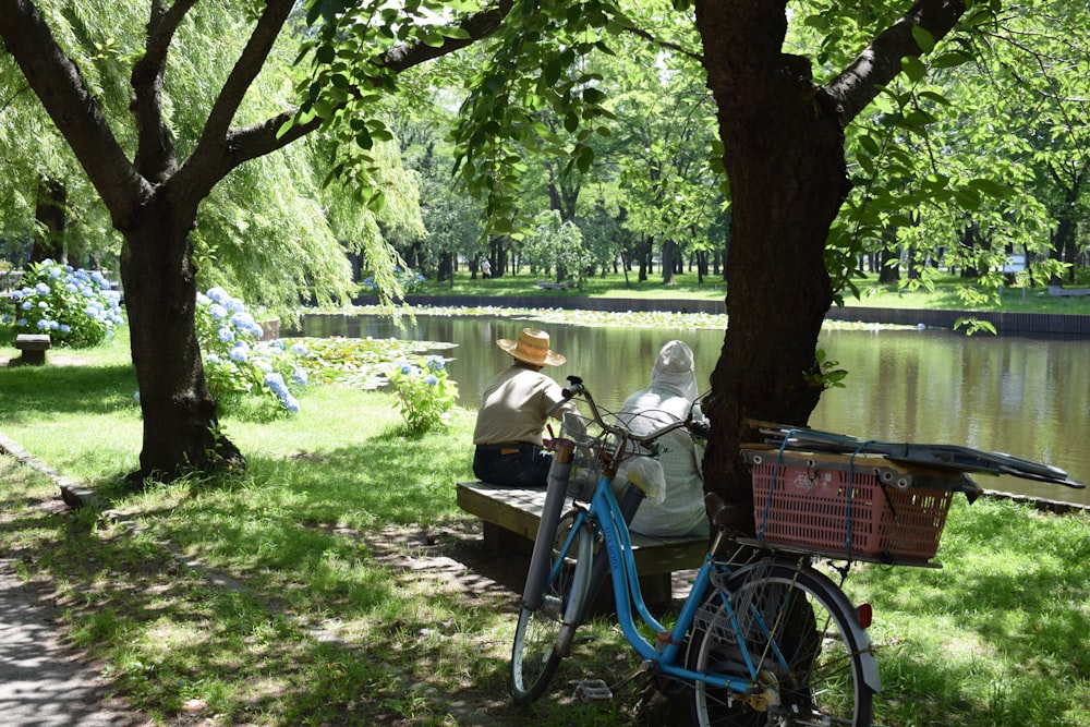 Frau im weißen Langarmhemd sitzt tagsüber auf blauem Fahrrad in der Nähe eines grünen Baumes