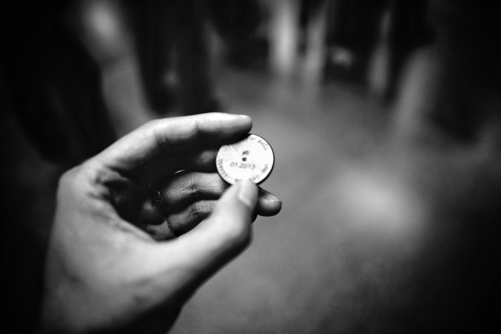 fotografia in scala di grigi di una persona che tiene in mano una moneta