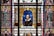 A detailed stained glass window depicts various figures associated with Shakespeare's works. In the center is a portrait of Shakespeare himself, surrounded by colorful, intricate patterns and designs. On either side are characters from his plays, including Juliet and Lady Macbeth. The artwork is rich in symbolism and ornate detail, conveying a sense of grandeur and reverence for the literary figures.
