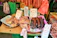 A market stall displaying an assortment of dried foods, including fish, sausages, and other meats. Handwritten signs with prices are visible, written in Chinese characters. The stall background includes green elements and various hanging items, contributing to a bustling market atmosphere.