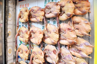 A display of several raw, plucked ducks hanging vertically on metal hooks against a background of signage with Chinese characters.